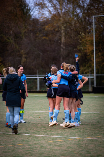 A group of young ladies on a field wearing blue uniforms, one of them holding a phone with the date 2023-11-19 written on it.