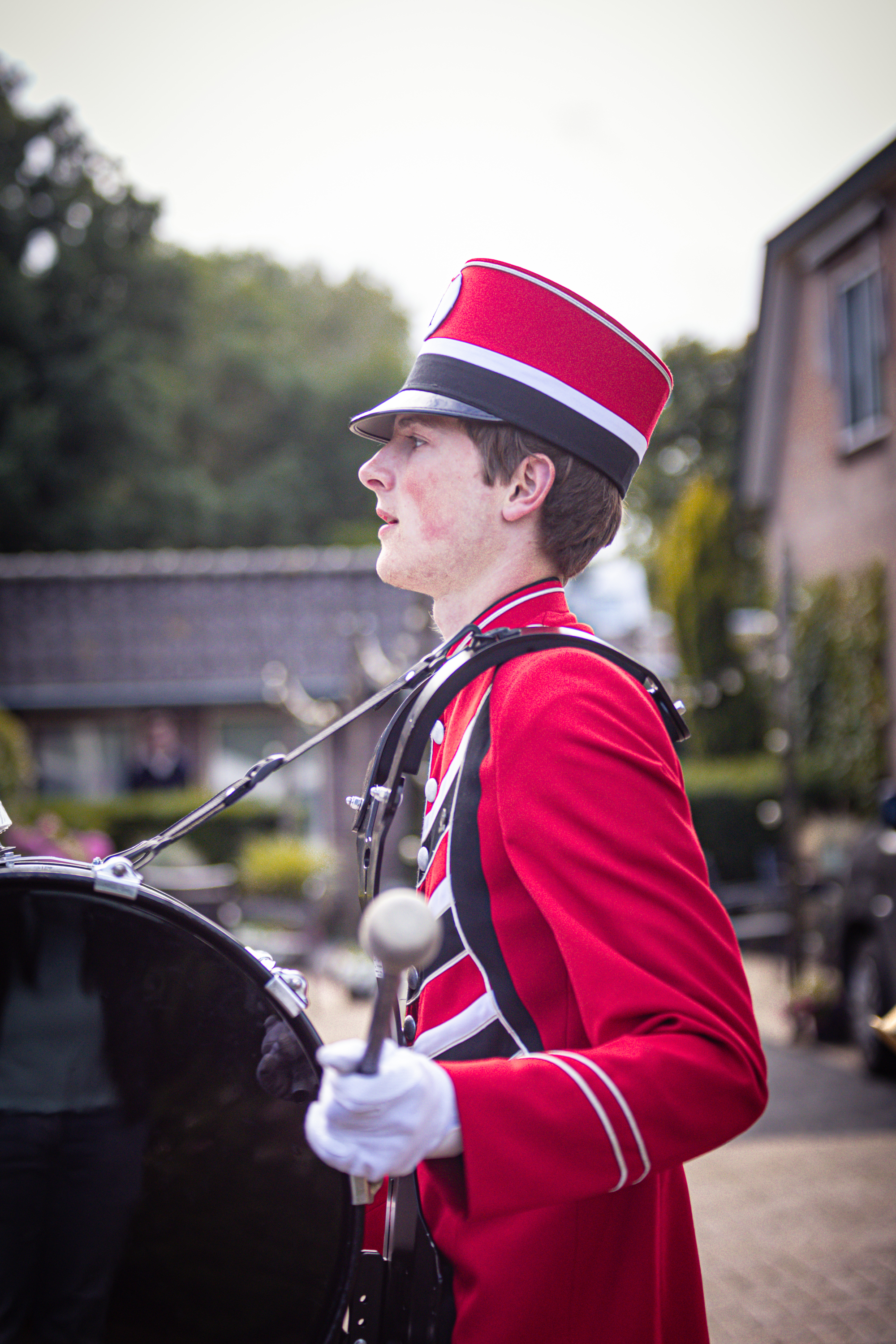 A young man wearing a red uniform with white stripes and a matching red hat is playing the drums.