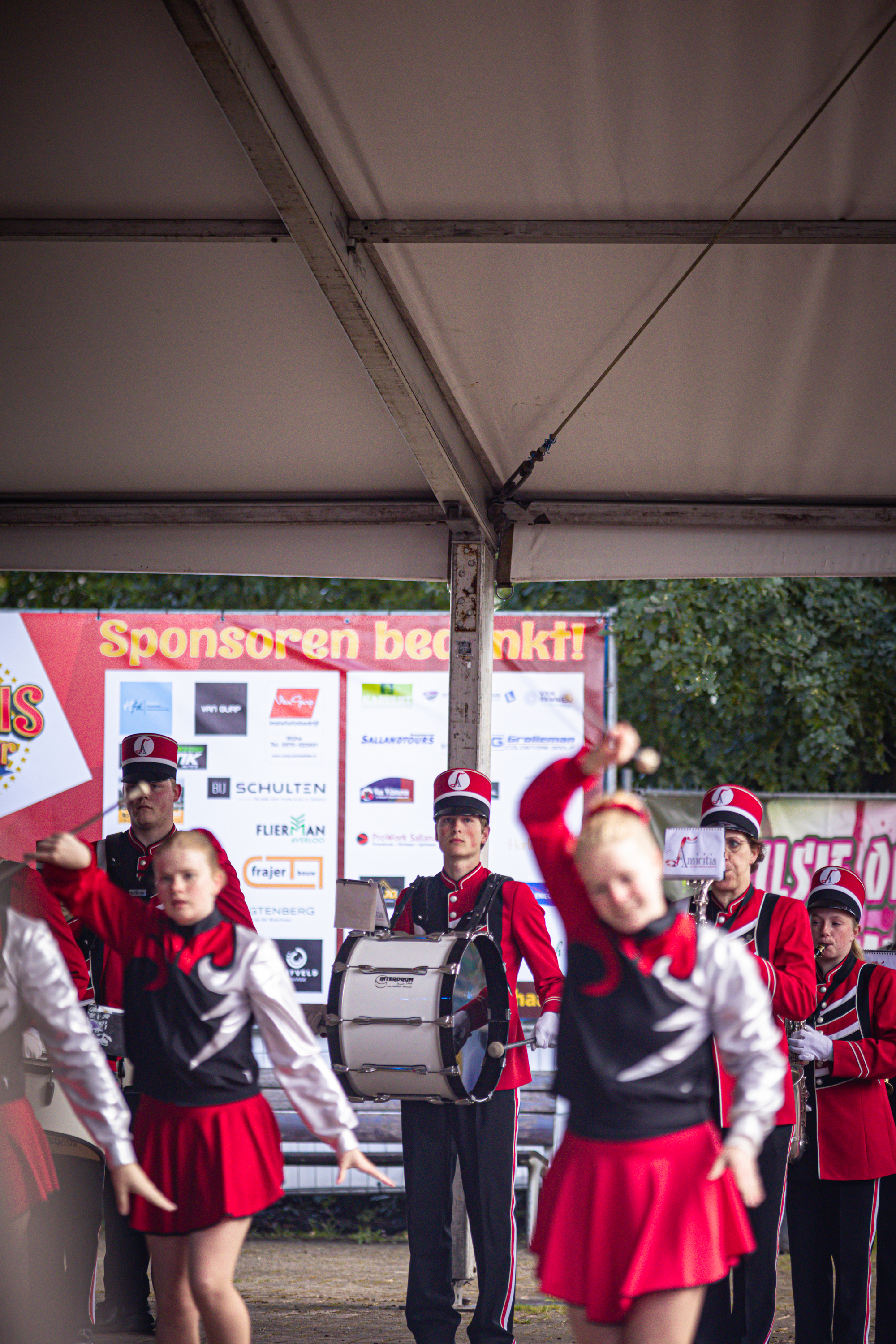 A group of children in red and black uniforms playing a band on stage with one child waving.