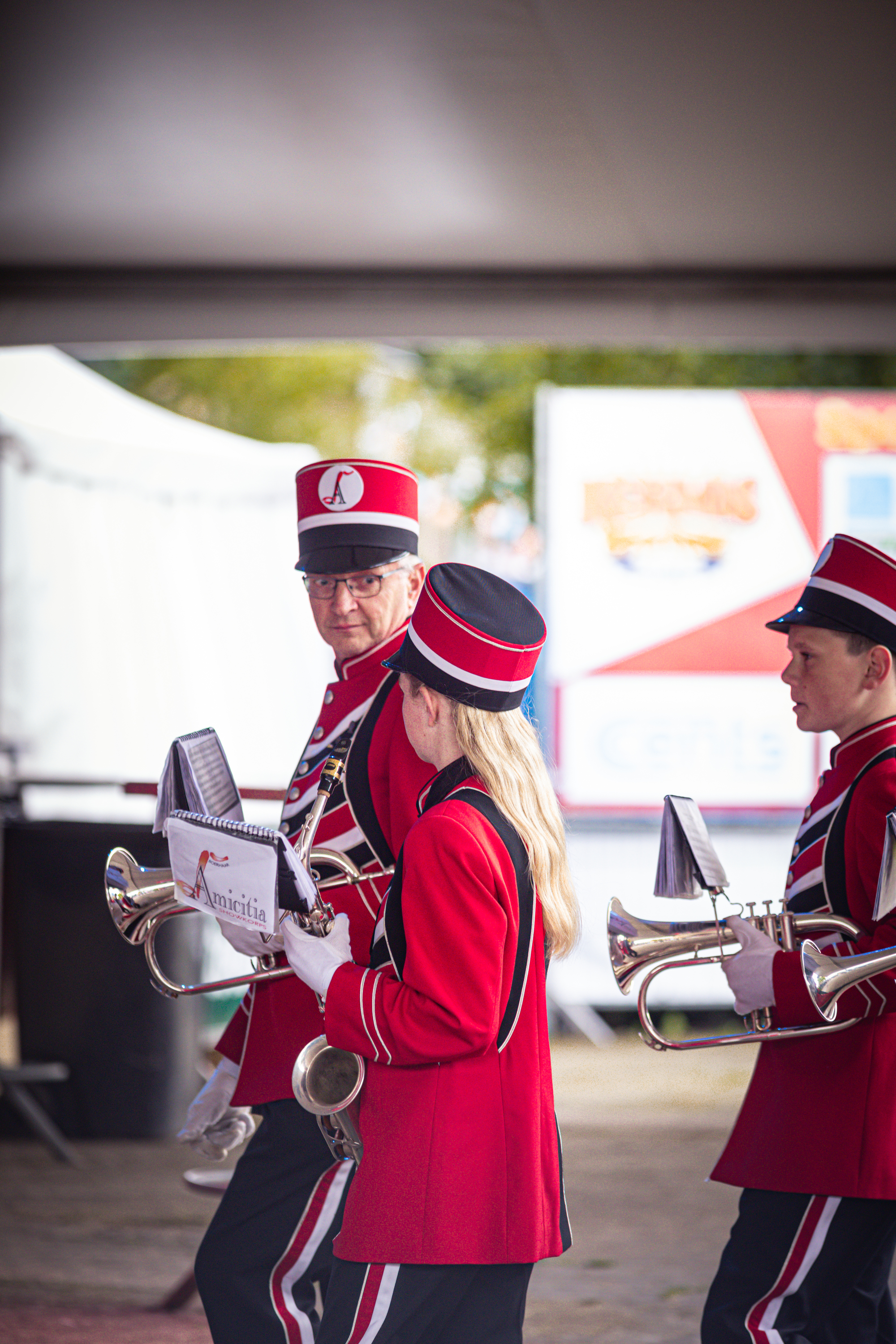 A group of musicians in red and black uniforms are playing brass instruments on a street.