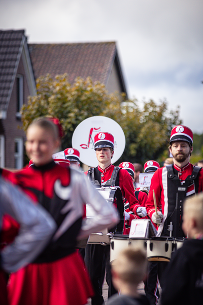 A group of people in red and white uniforms are playing drums on a street at an event.