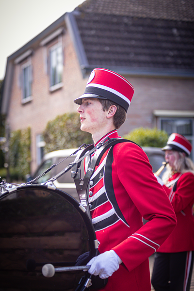 A young boy in a red and black marching band uniform stands with his drum.