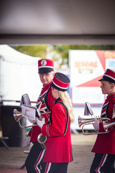 A group of musicians in red and black uniforms are playing brass instruments on a street.