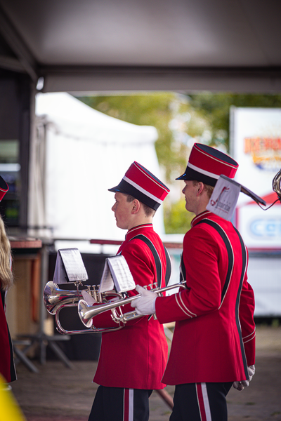 Two men in red and white marching band uniforms are carrying brass instruments.