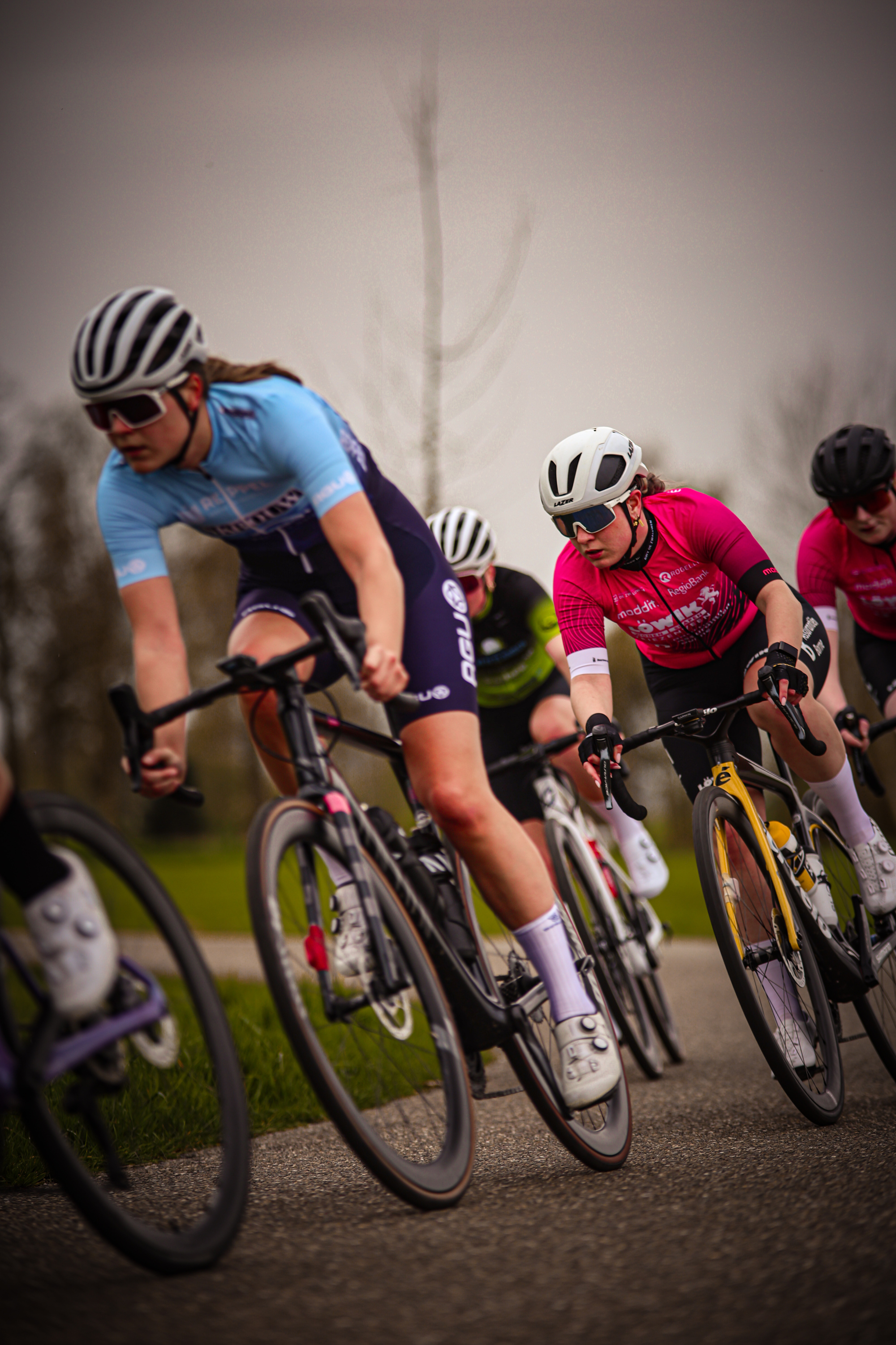 A group of female cyclists race down a road on a cloudy day.