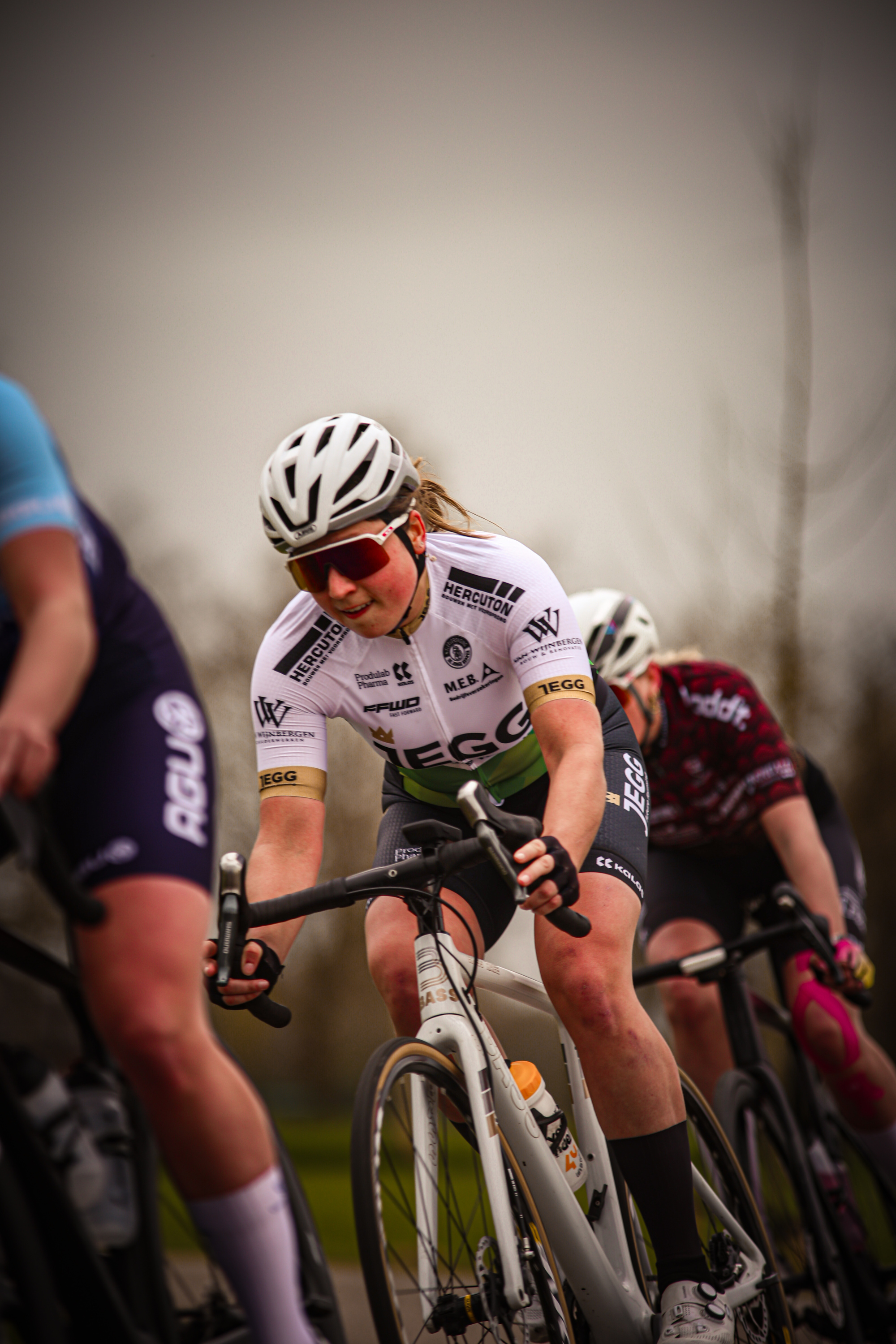 A female cyclist is wearing a black jersey with the word "wielrennen" on it. She is riding in a race during daylight hours.