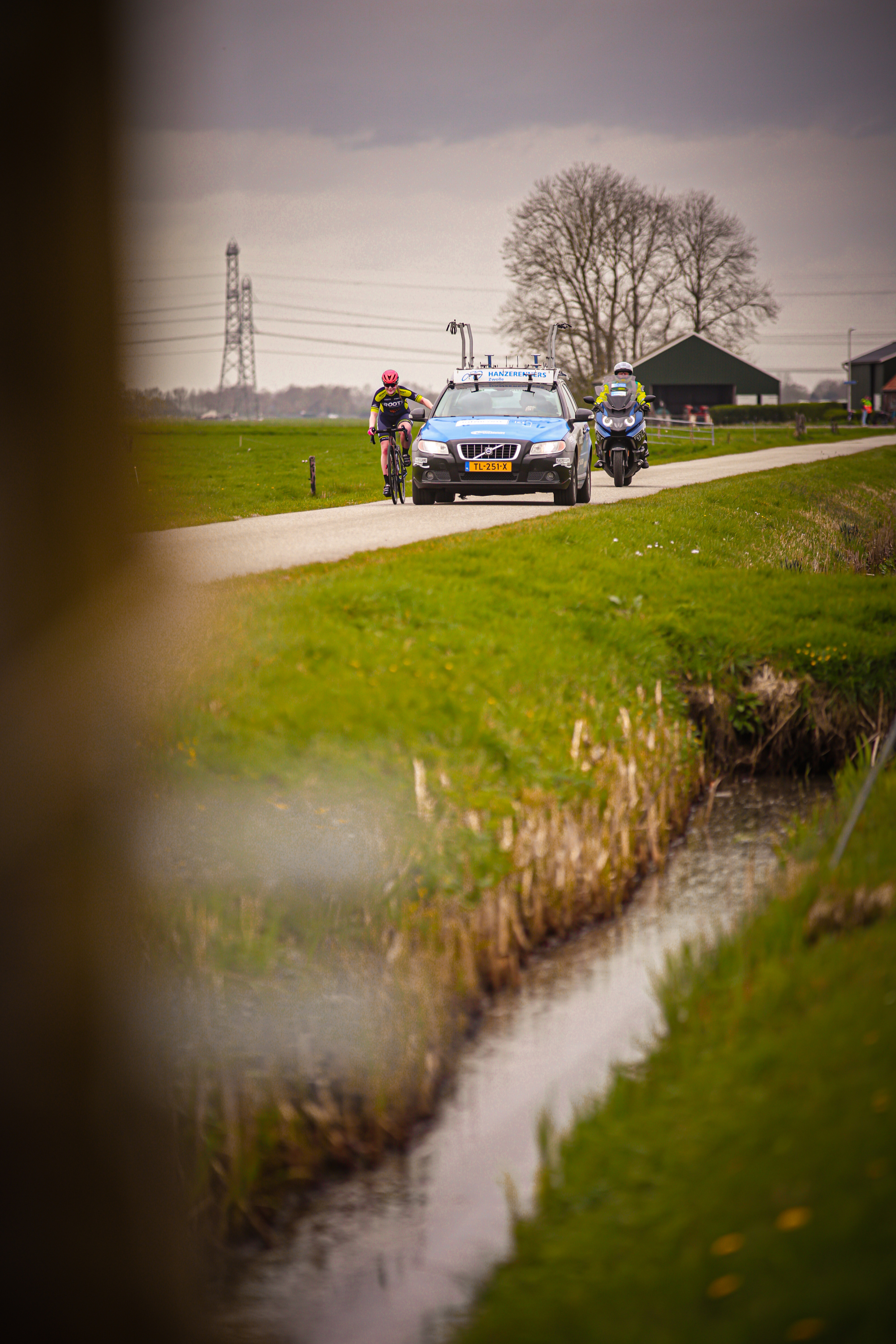 A cyclist and a motorcycle are following another cyclist on a road during the Ronde van de Lichtmis race.