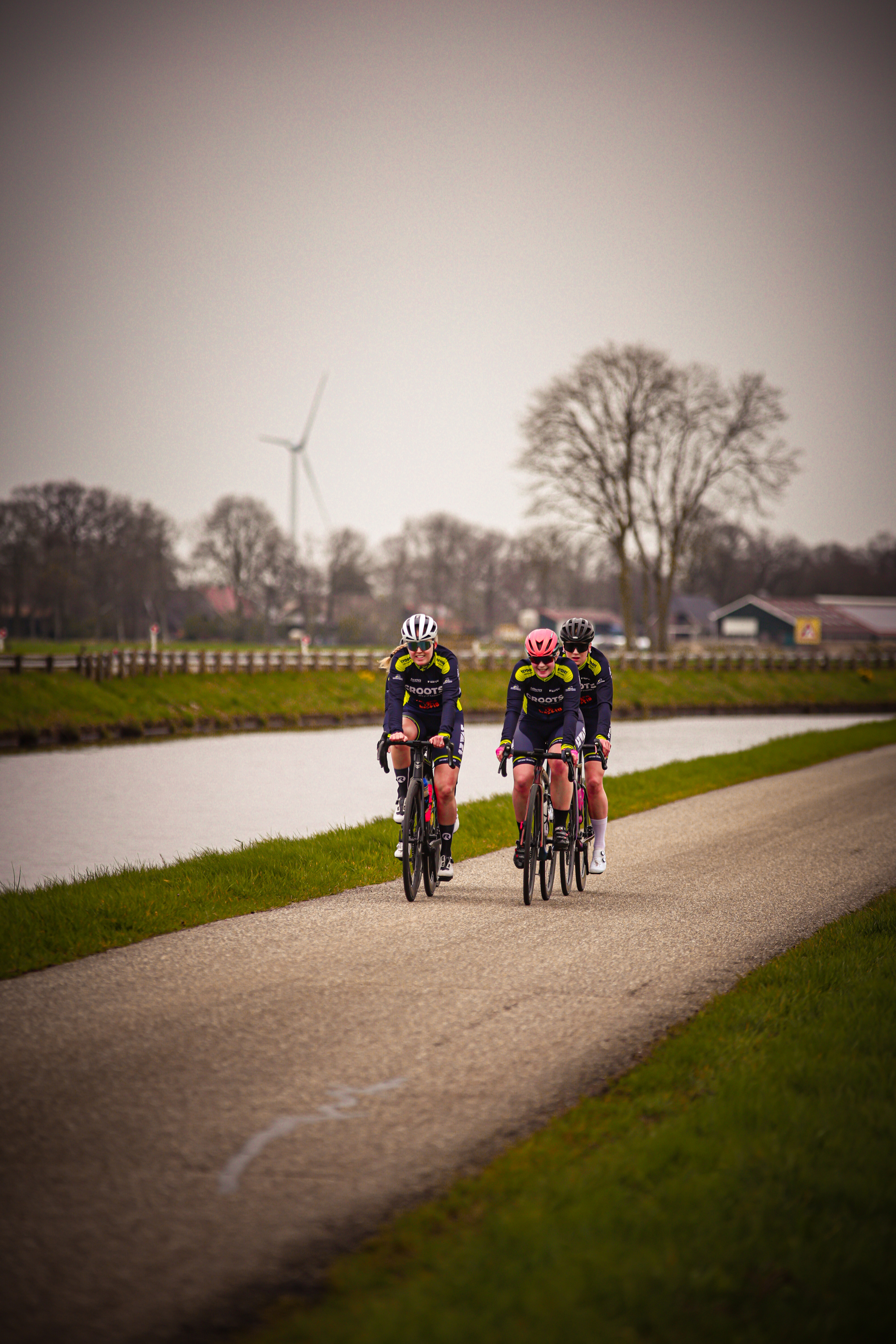 Three cyclists riding on a gravel road. They are wearing helmets and have the number 1 on their jerseys.