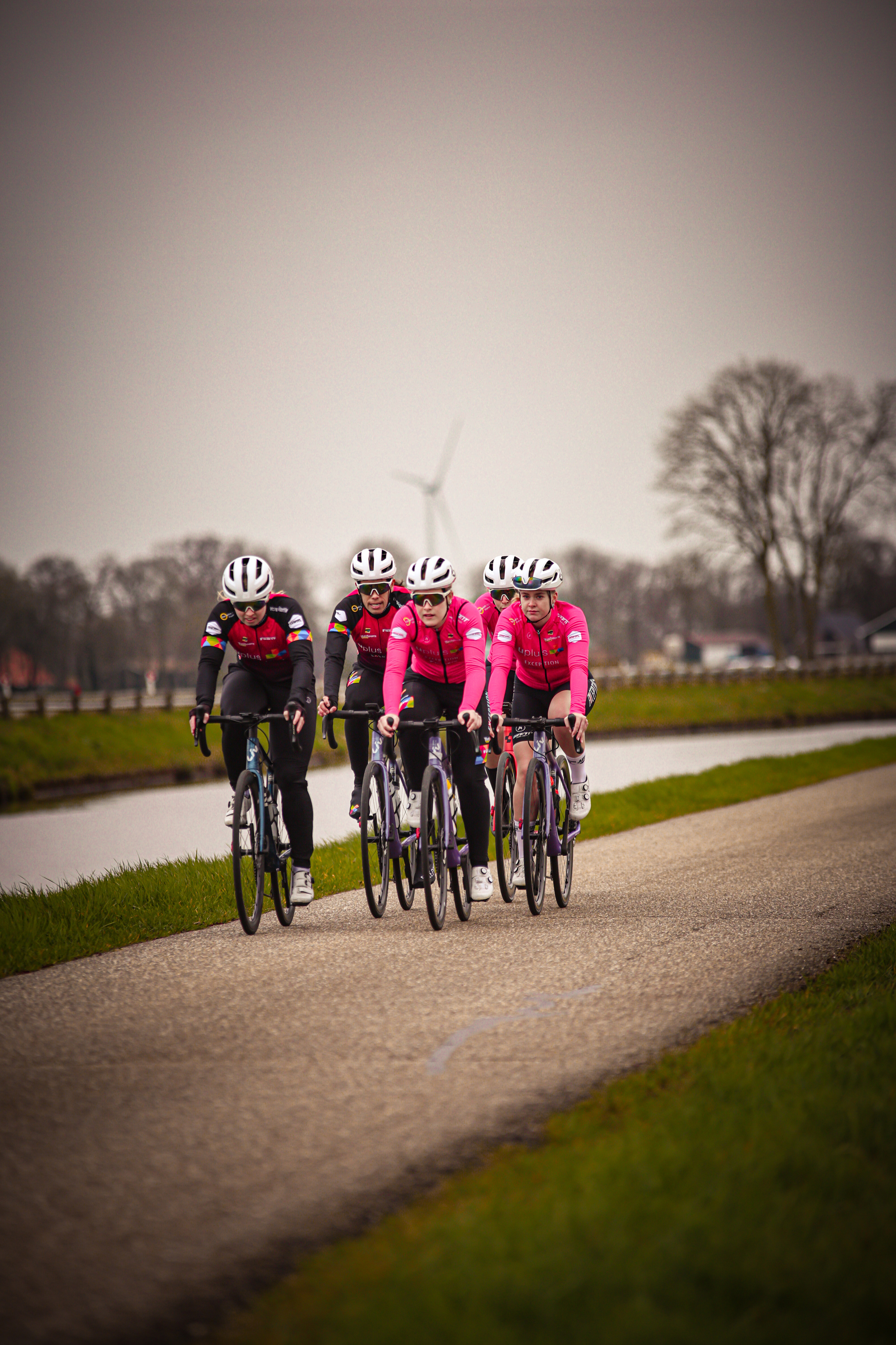 A group of four cyclists wearing red and black riding down a road.