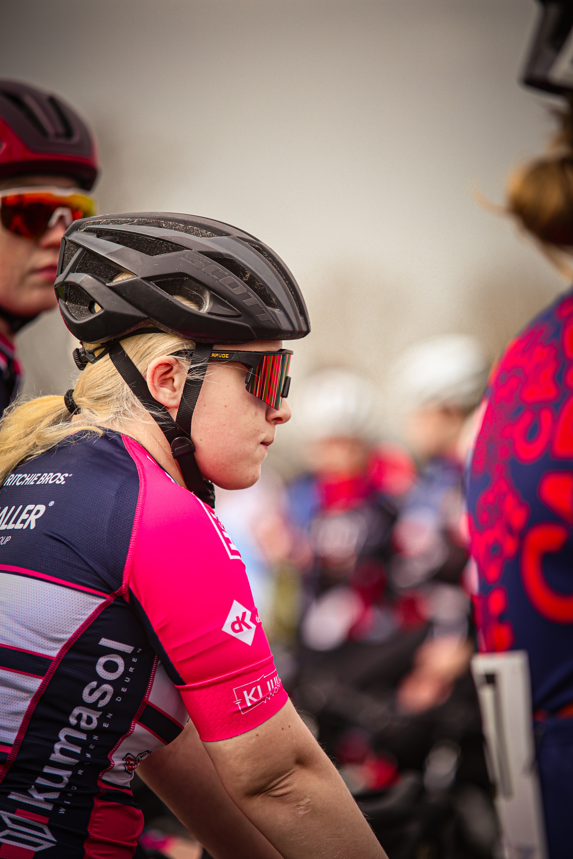 Two women wearing helmets with bikes are part of a group of cyclists.