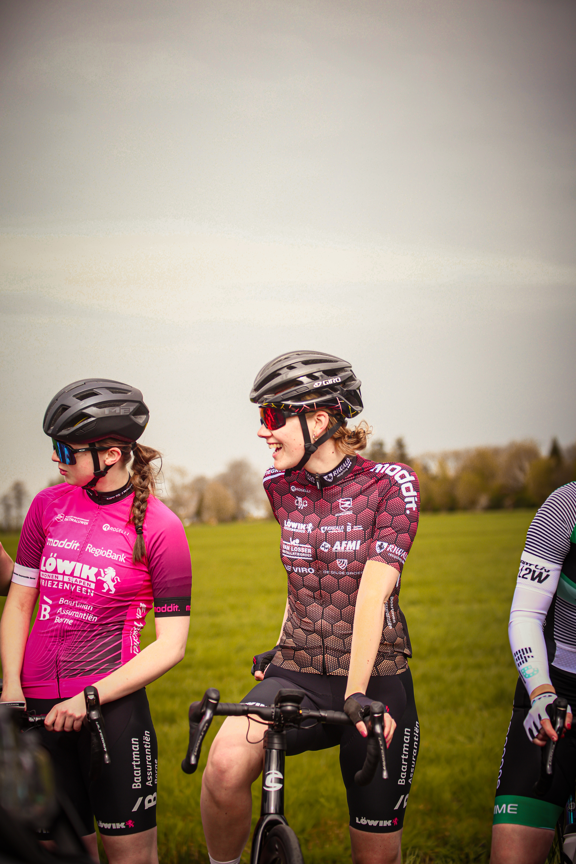 Three cyclists on a field with one in pink and two in black.