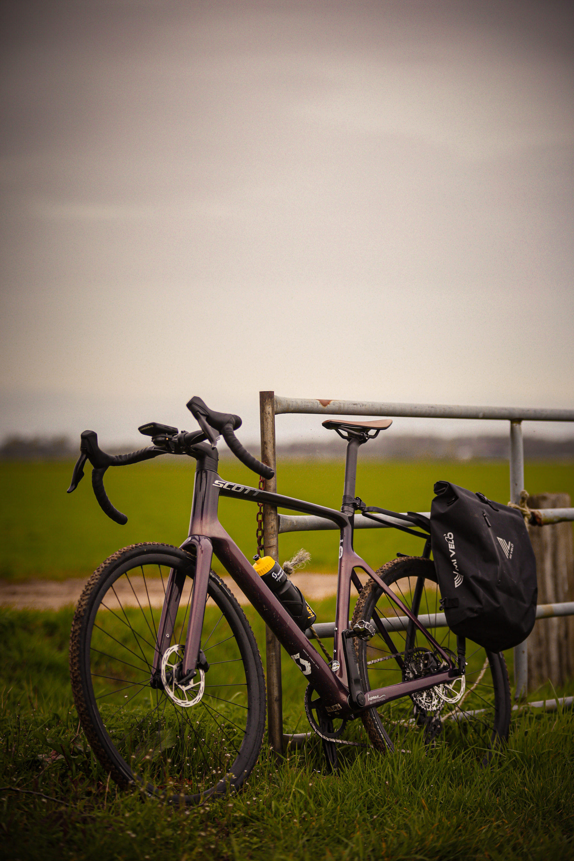 Two bicycles leaning on a fence in a grassy field.