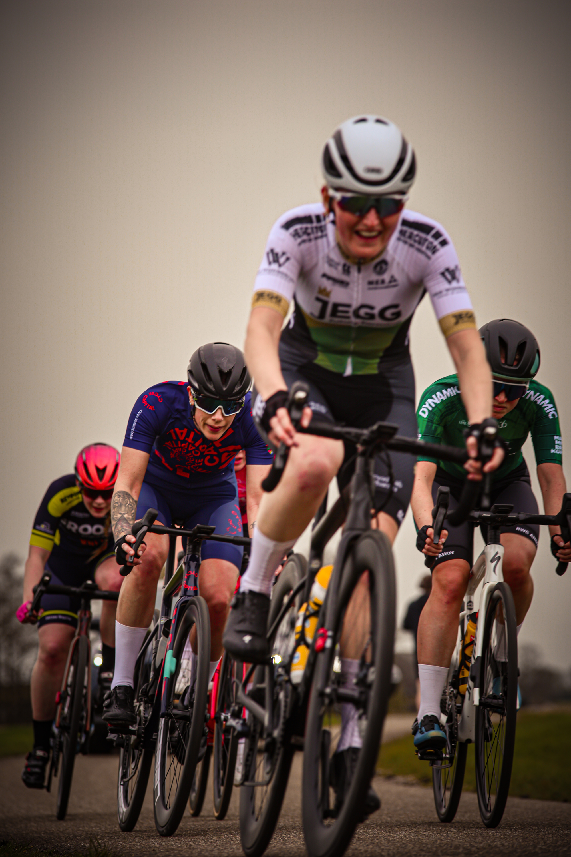 A group of bicyclists racing during the Ronde van de Lichtmis, with a man leading in first place and wearing a green jersey.