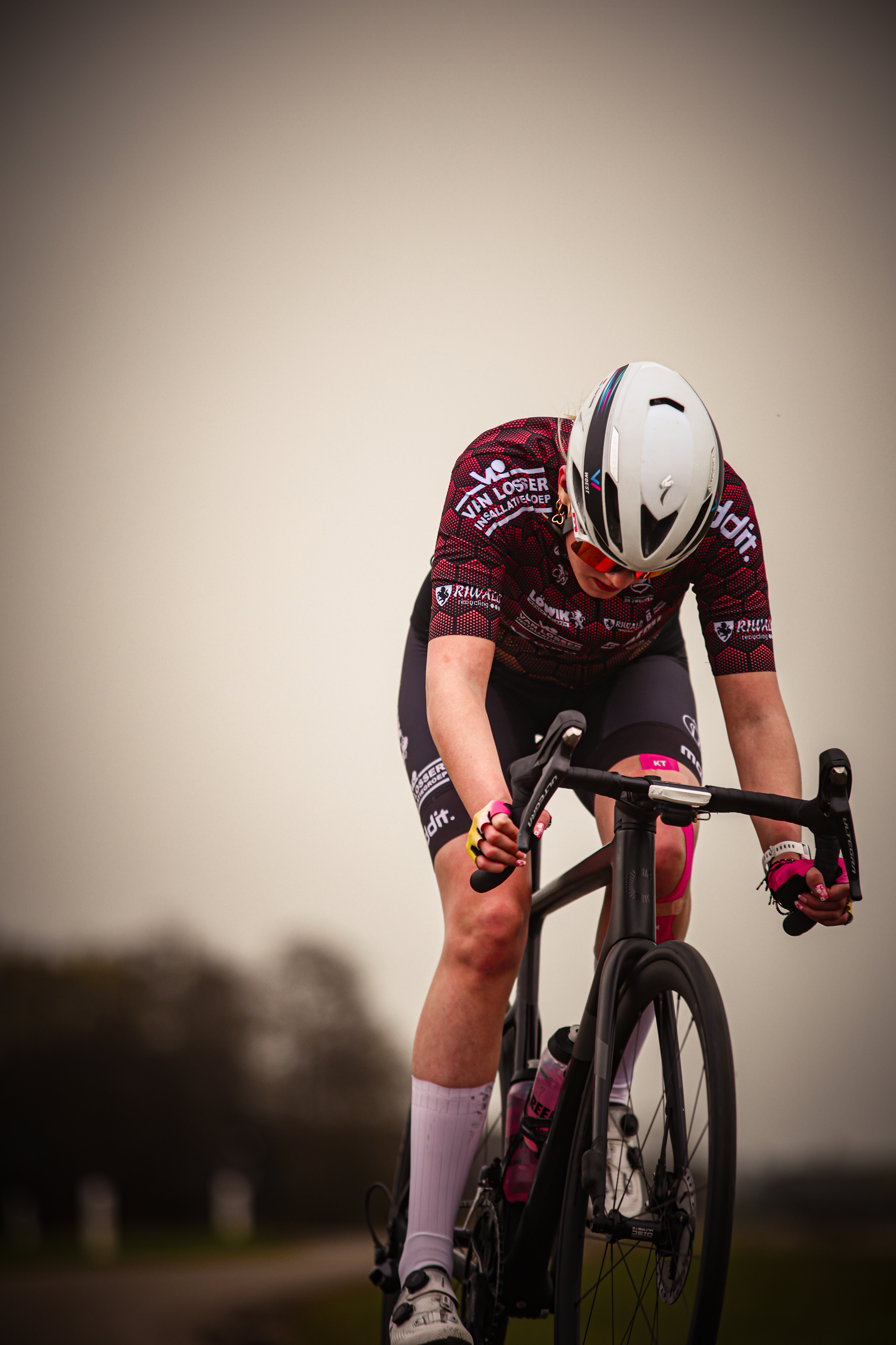 A woman wearing a red, black and white shirt rides her bicycle in the Ronde van de Lichtmis.