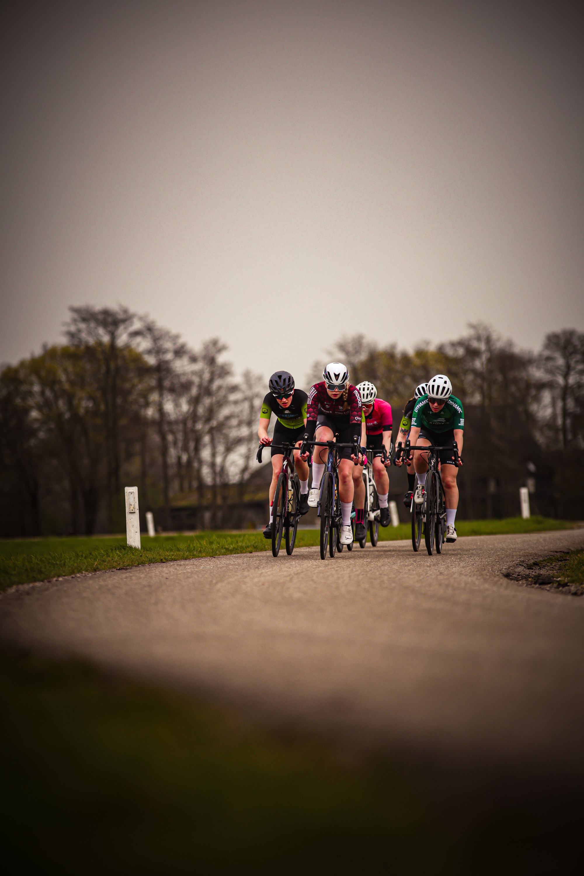 Three cyclists on a road with the first two wearing helmets.