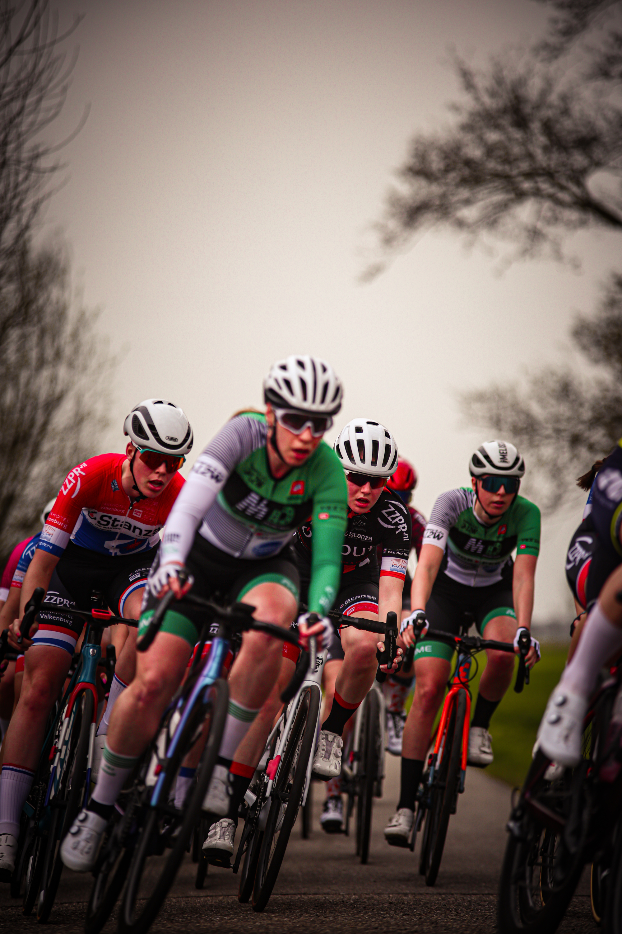 A group of cyclists wearing green and white outfits are riding down a street.