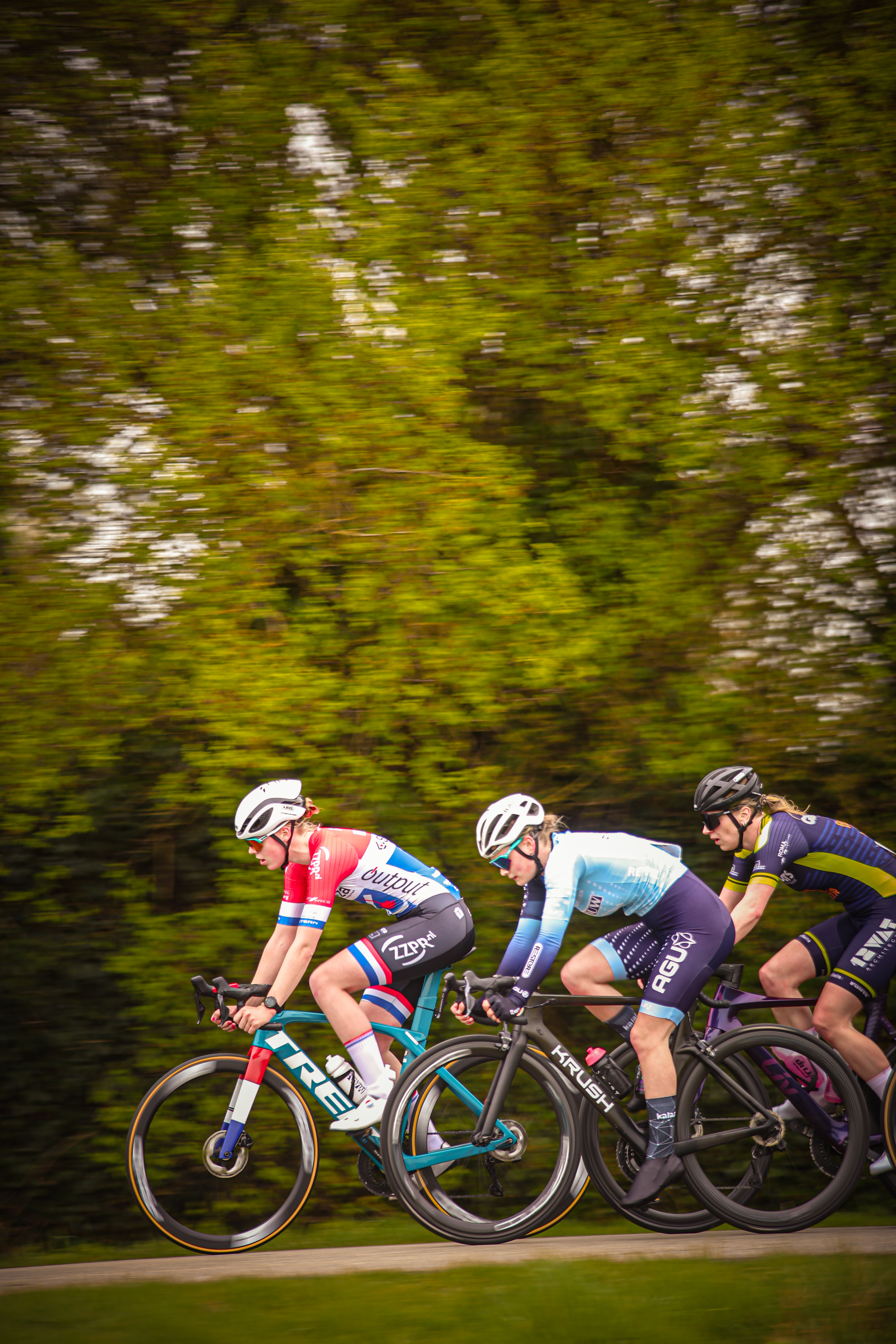 Three cyclists racing down a road with a red, white, and blue jersey wearing the number 6 leading the pack.