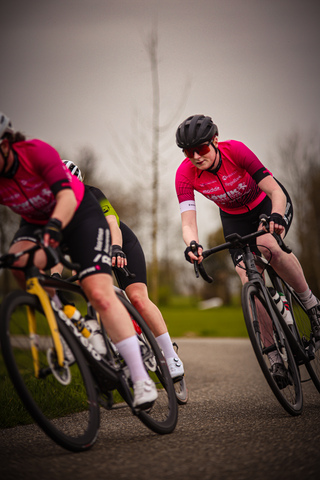 Two women on bikes wearing pink and black clothes.