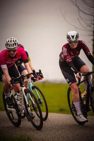 Two female cyclists, one in a black and red jersey and the other in pink.