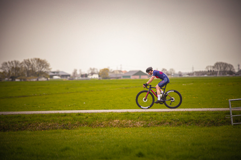 A bicyclist wears a blue and red jersey while riding a black and orange bike.