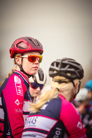 Two women wearing matching pink and blue cycling outfits stand together at a cycling event.