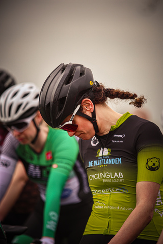 A woman, dressed in a black and green cycling jersey, is wearing a blue helmet.