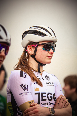 A woman in a sports uniform stands against a white wall.