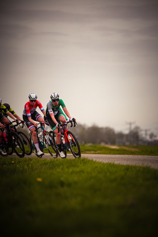 Two cyclists on a road with one wearing a green shirt and white helmet.