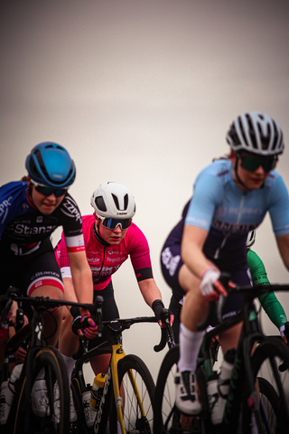 A woman wearing a blue and white shirt is riding a bike in a group of three people. They are all wearing helmets.