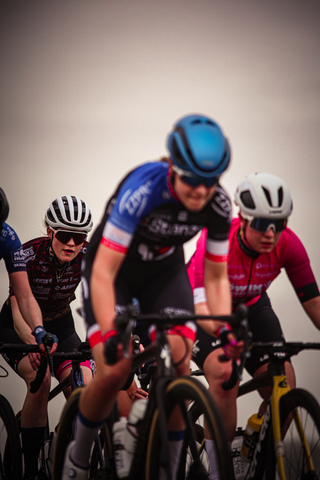 Three cyclists on a race track with white helmets and blue and red jerseys.