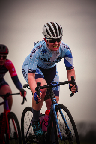 A cyclist is riding her bike through a race, wearing sunglasses and a helmet for safety.