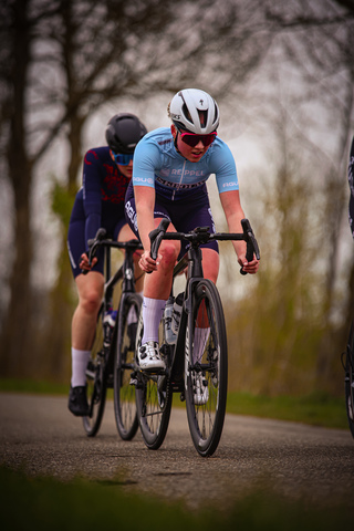 Two female cyclists are racing down a road on a cloudy day.