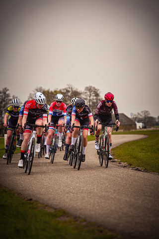 A group of cyclists wearing red and blue uniforms ride down a gravel road during the Ronde van de Lichtmis.