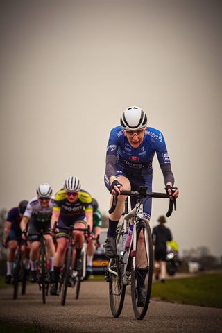 Four cyclists are riding on a path, one of them wearing a blue jersey with the words "Ronde van de Lichtmis".