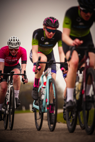 Three women wearing helmets are racing on bicycles.