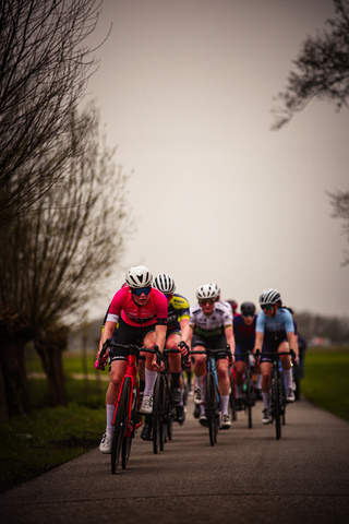 A group of cyclists on a paved road with a grassy field in the background.