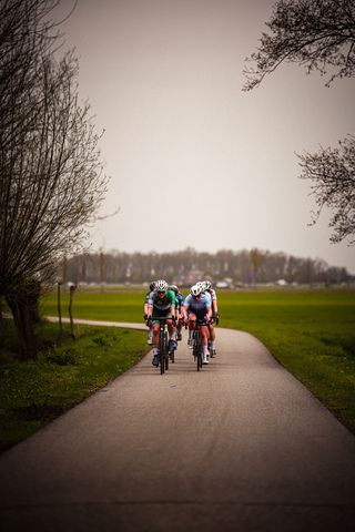 A group of cyclists ride down a street on a cloudy day.