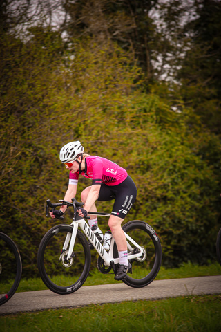 A cyclist in a pink jersey is riding her white bike.