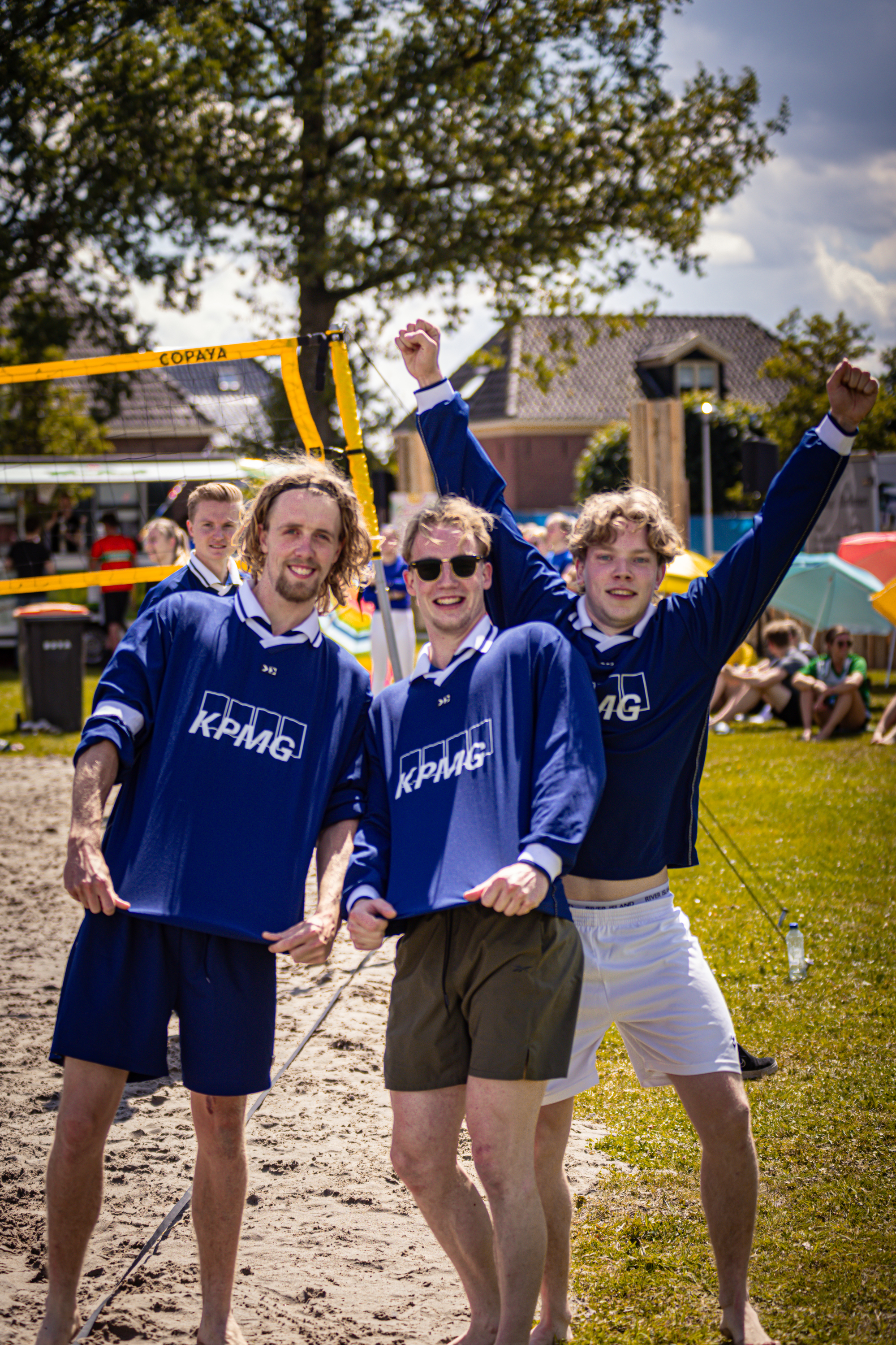 Three men dressed in blue are playing beach volleyball.