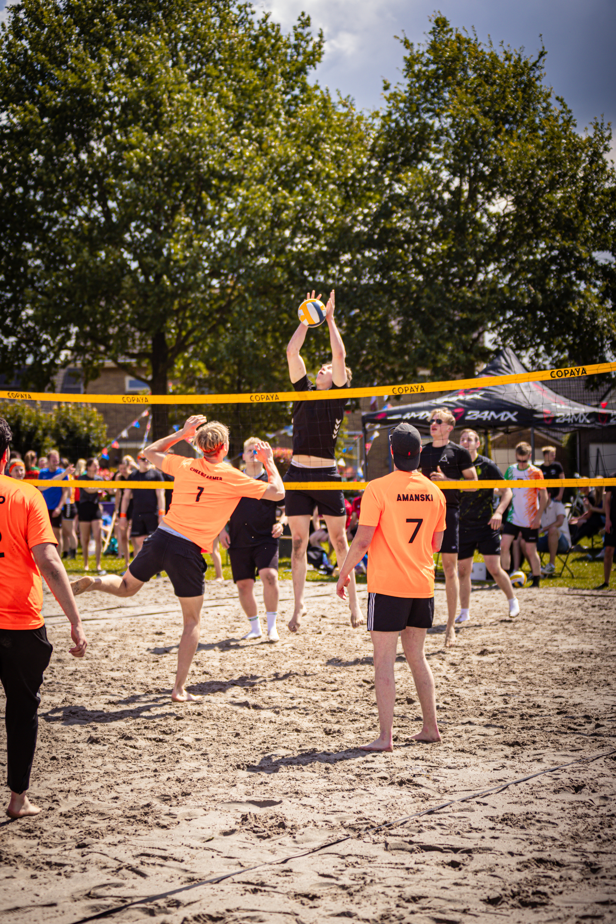 A group of people playing beach volleyball, two women are jumping up to hit the ball.