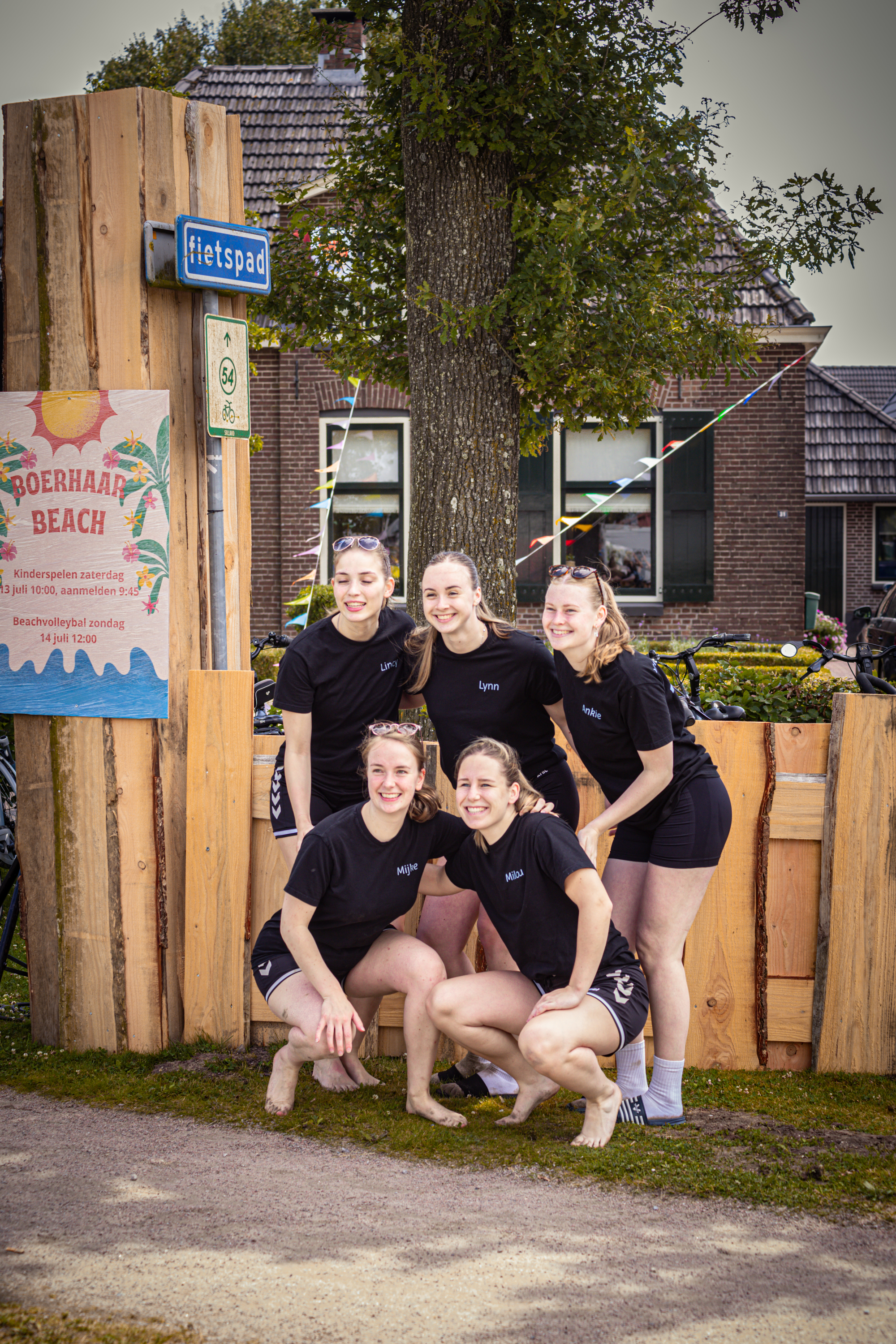 A group of six girls pose for a photo in front of a sign that reads "Beach Volleybal Kermis Boerhaar".