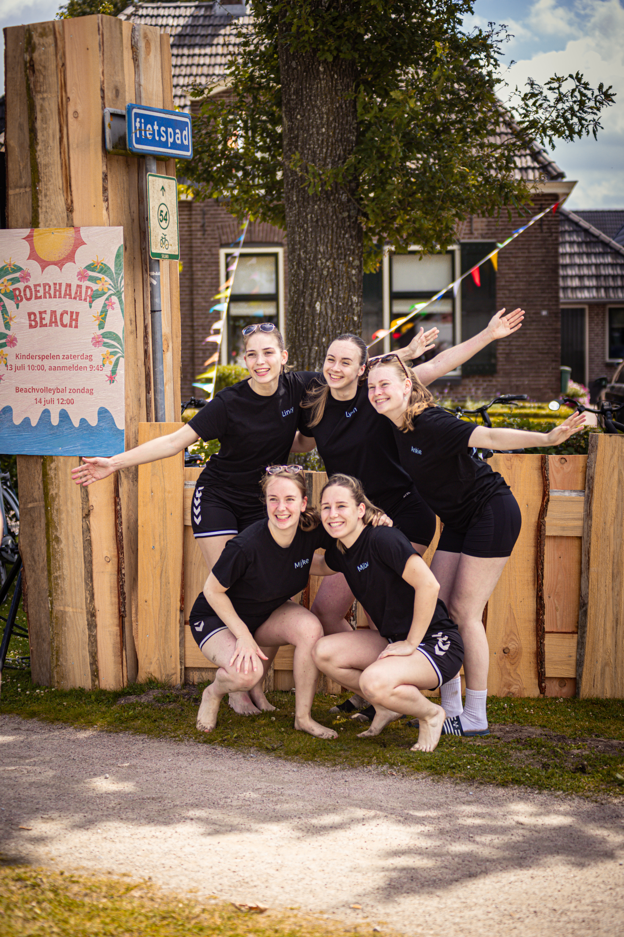 Four girls in black shirts and shorts posing for a photo with their arms up.