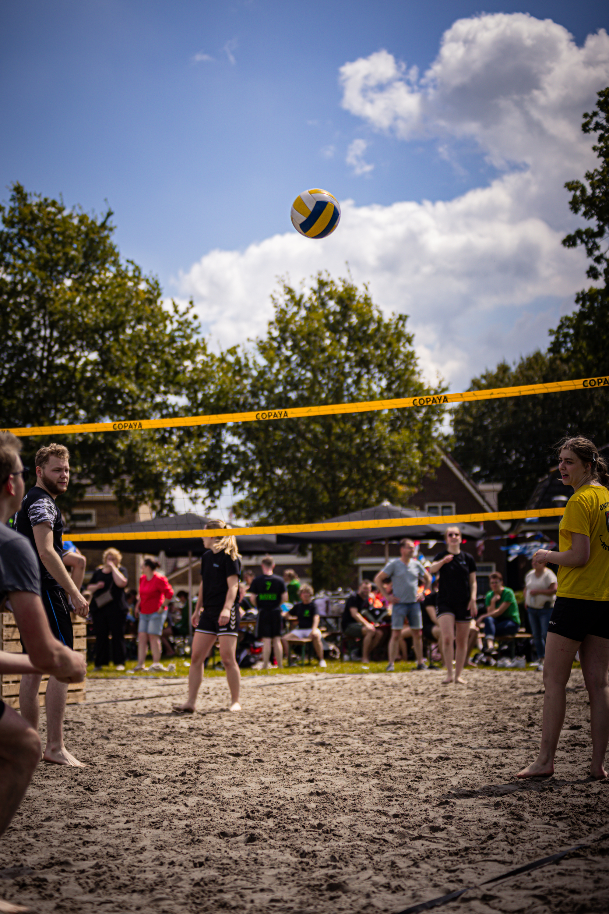 A group of people playing beach volleyball with a yellow and blue ball in the air.