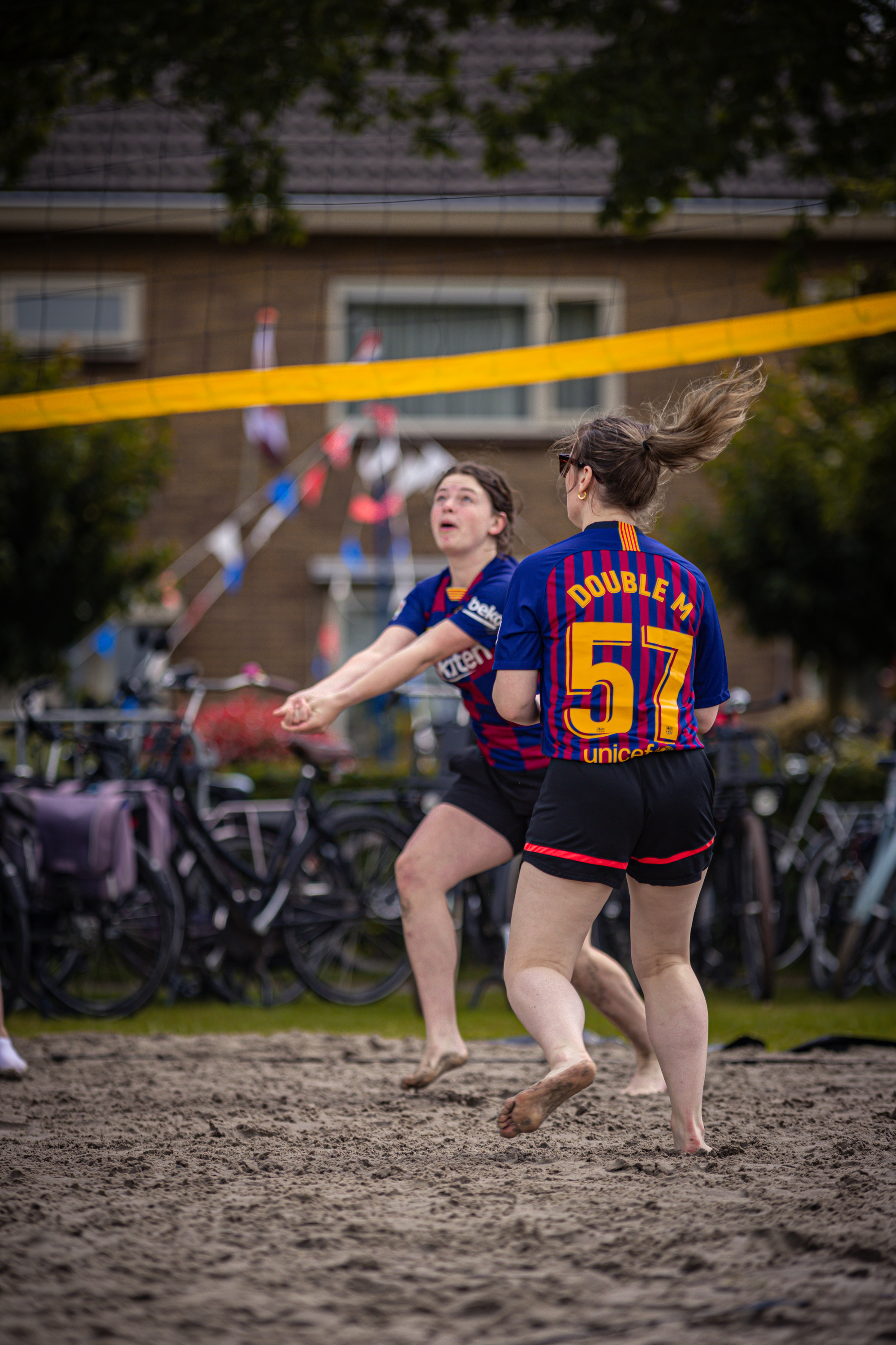 Two women are playing beach volleyball in a competition, the player with the blue jersey has the number 57 on it.