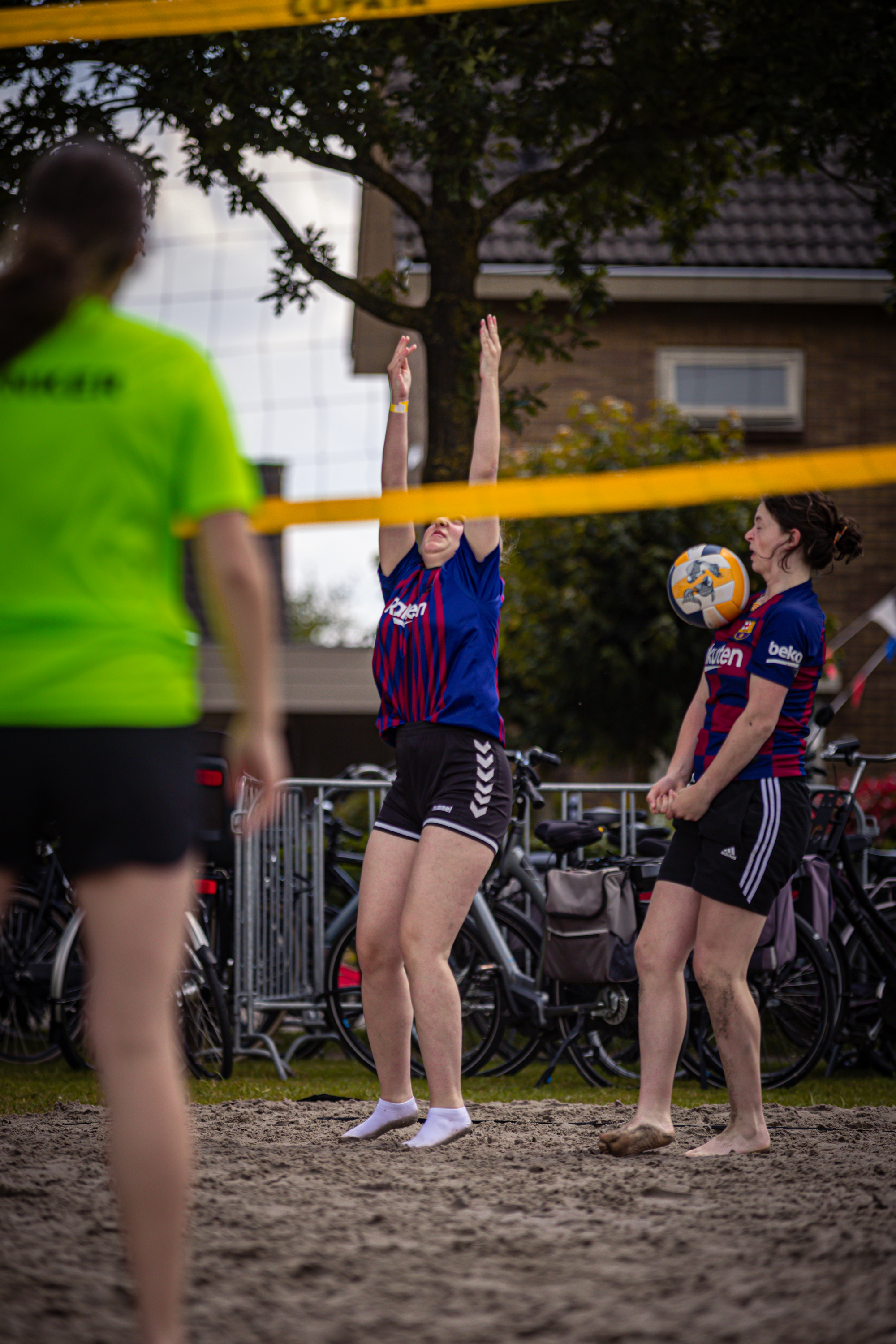 Three people on a beach with two volleyball jerseys and one ball.