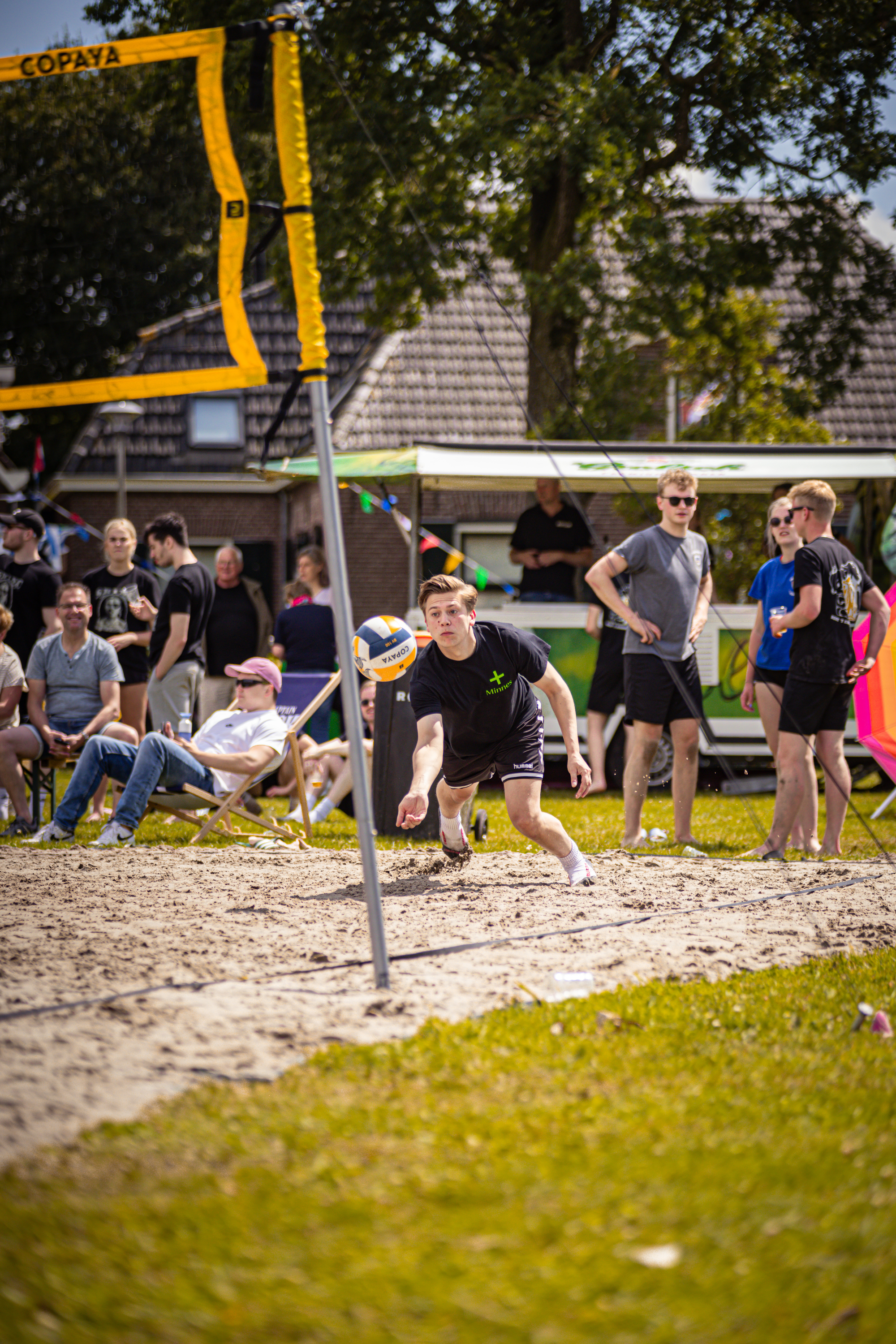 A man prepares to serve a beach volleyball in front of several people.