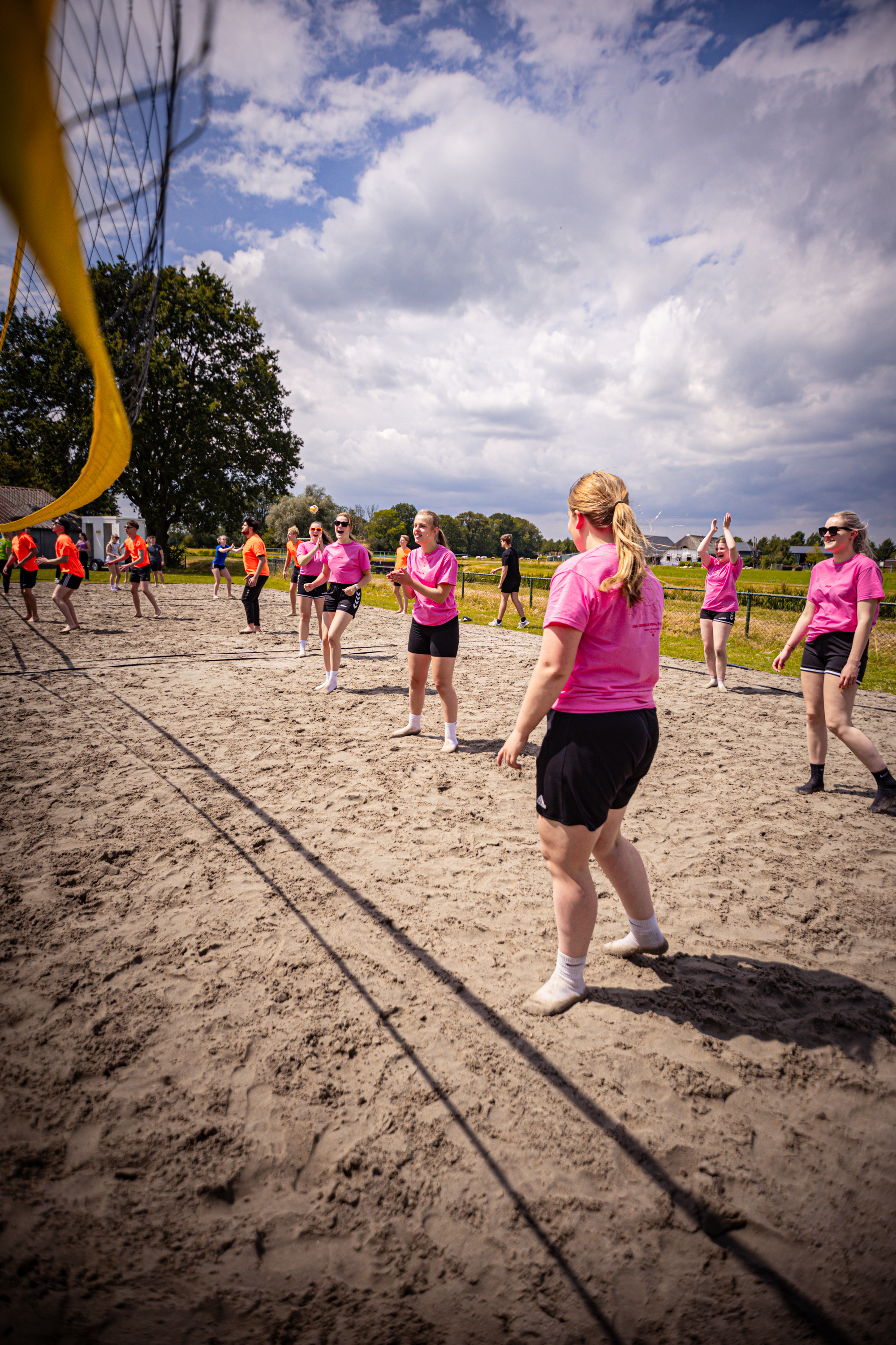 A woman wearing a pink shirt is playing volleyball with others on the beach.