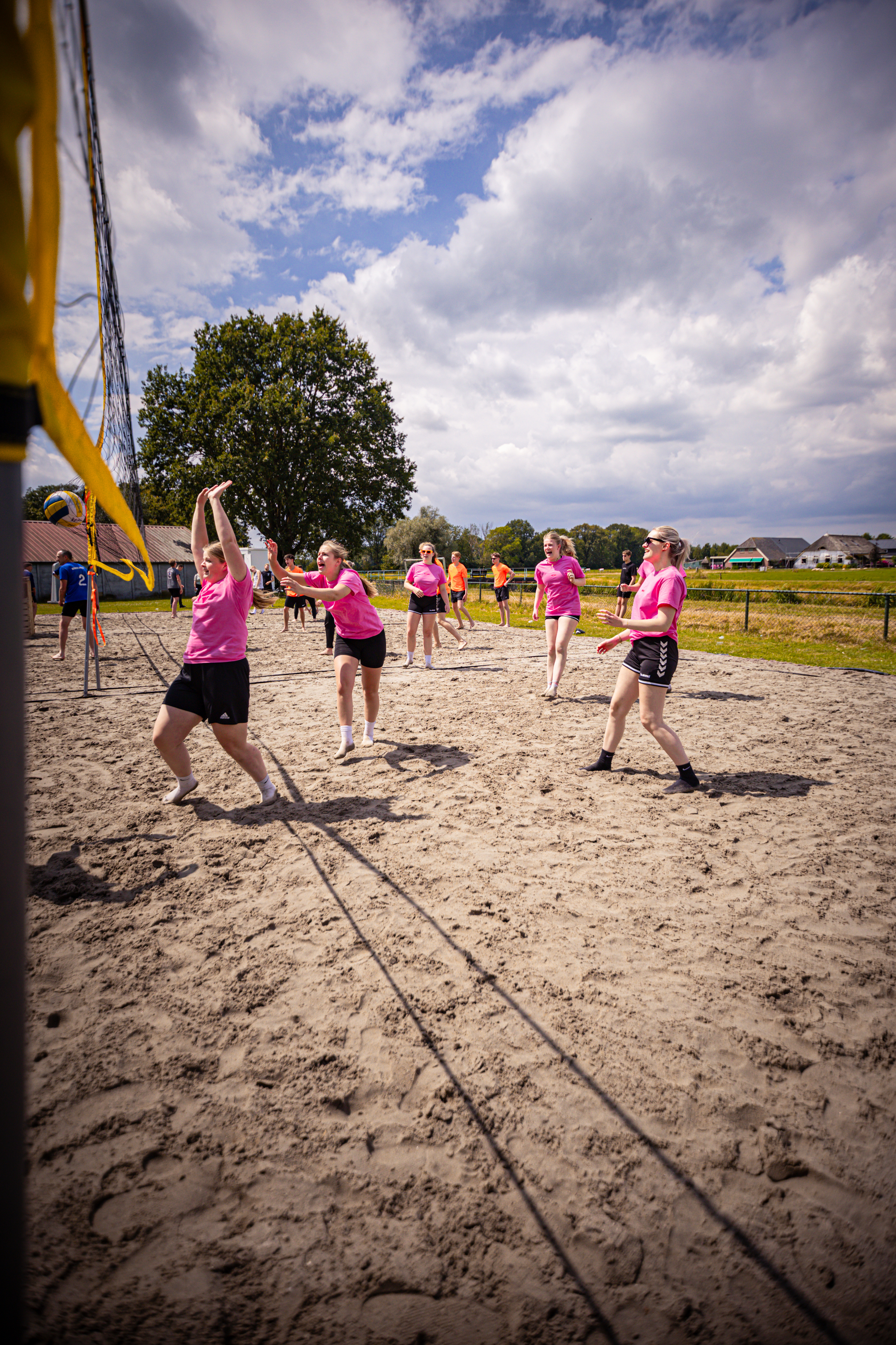 Six women in pink shirts are playing beach volleyball.