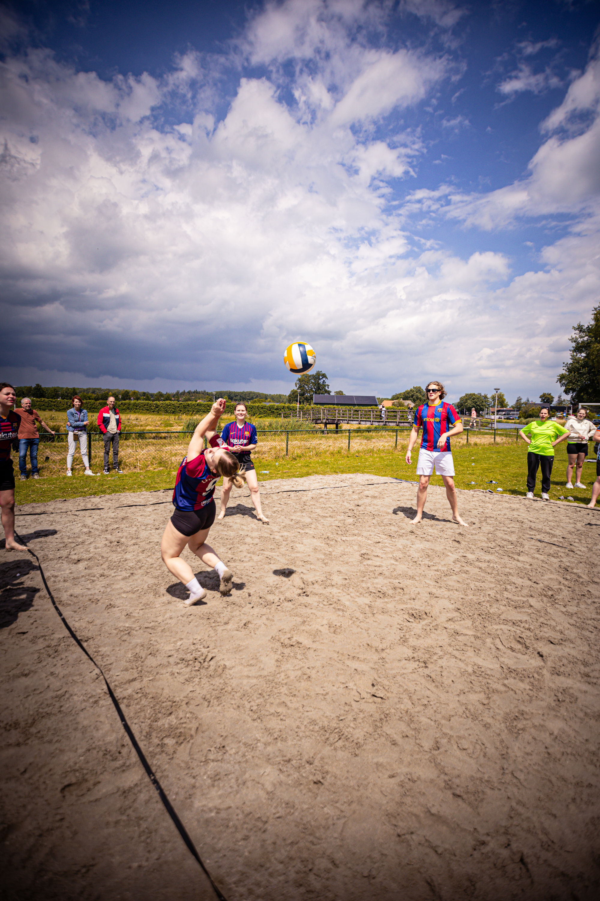 Beach volleyball game being played. The people are wearing different shirts, with one shirt saying "Kermis Boerhaar".