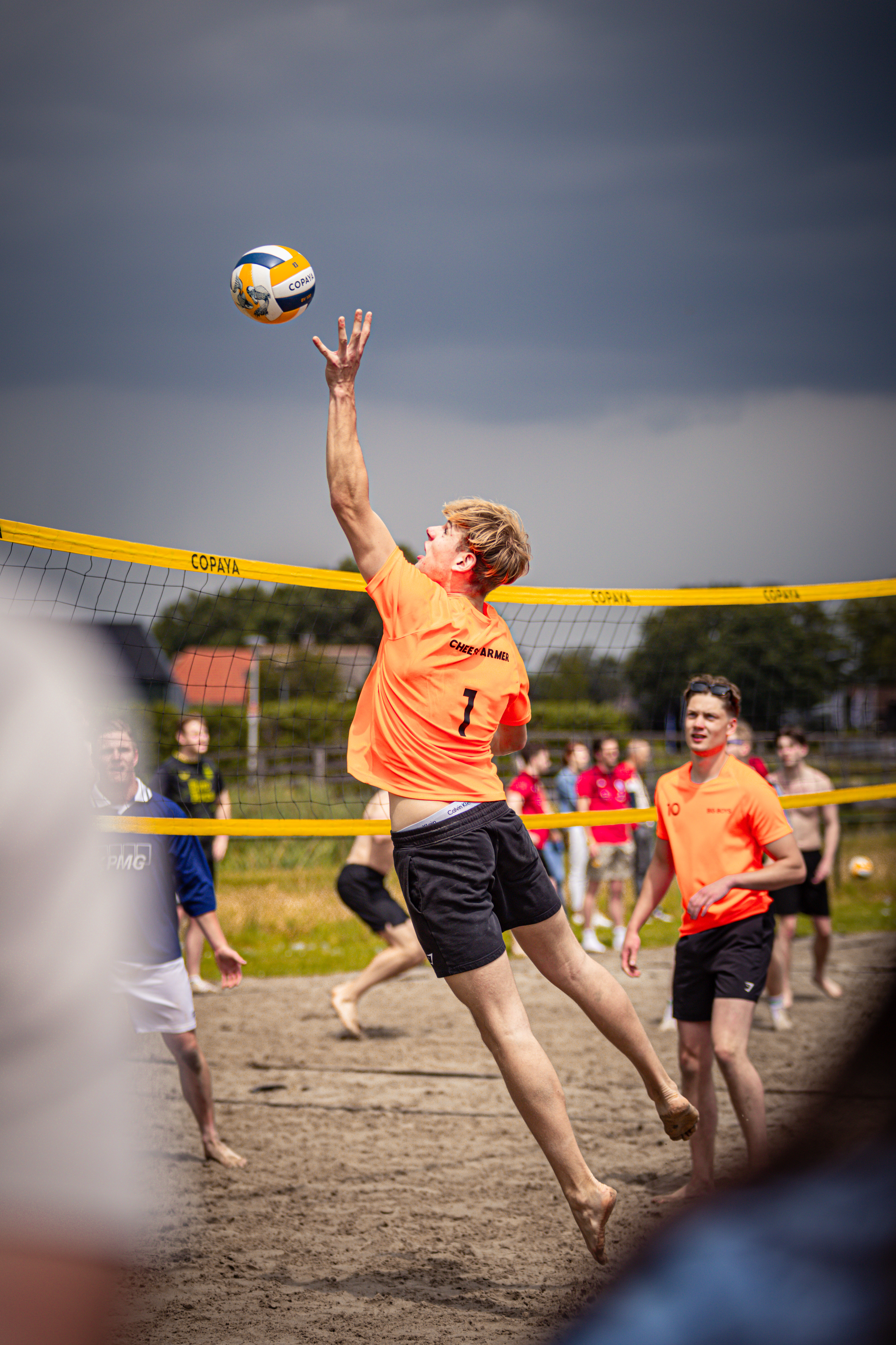 A volleyball player in a red shirt jumps to hit the ball, with several other players and spectators watching on.